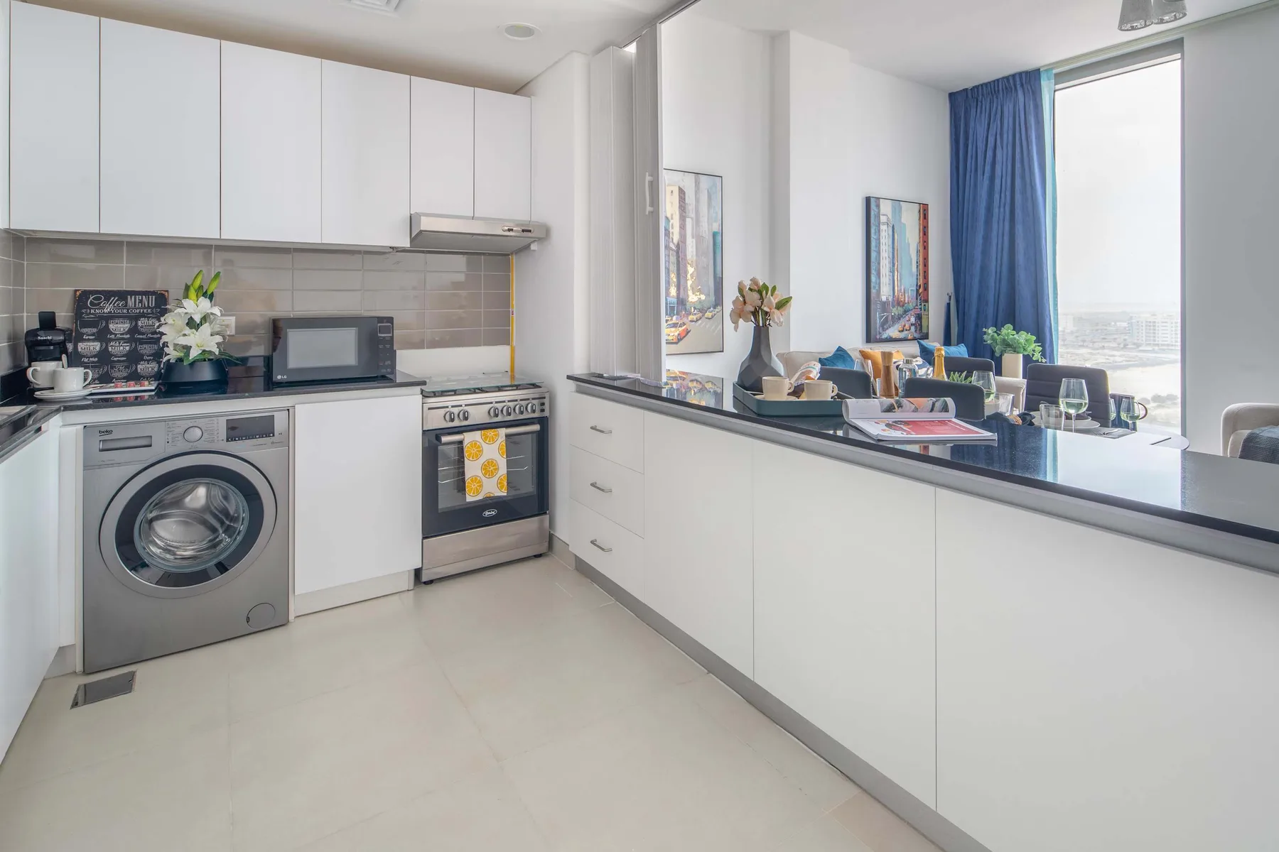 Una cocina moderna y luminosa con gabinetes blancos y una barra frente a la sala.