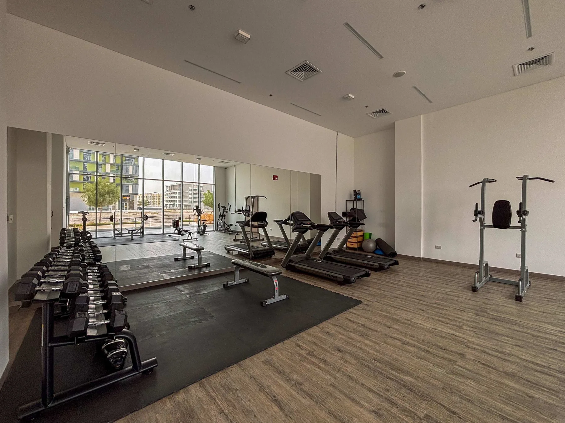 Un gimnasio con máquinas de ejercicio, pesas y grandes ventanales.