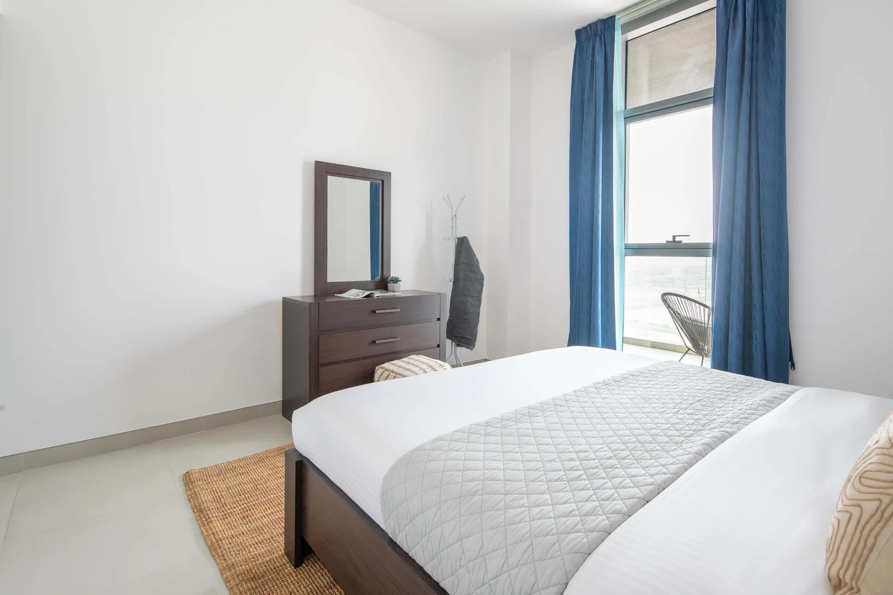 Un dormitorio luminoso con una cama bien tendida y una ventana con cortinas azules.