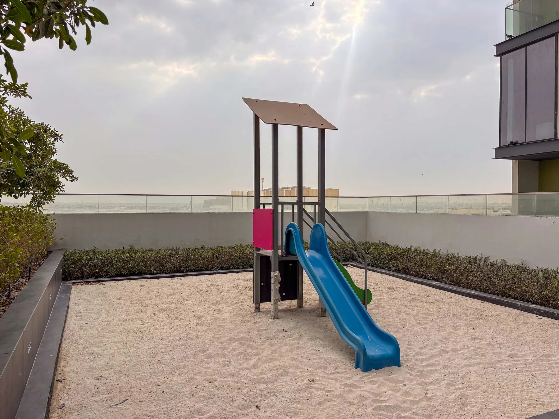 Un parque infantil al aire libre con un tobogán azul en una zona de arena.