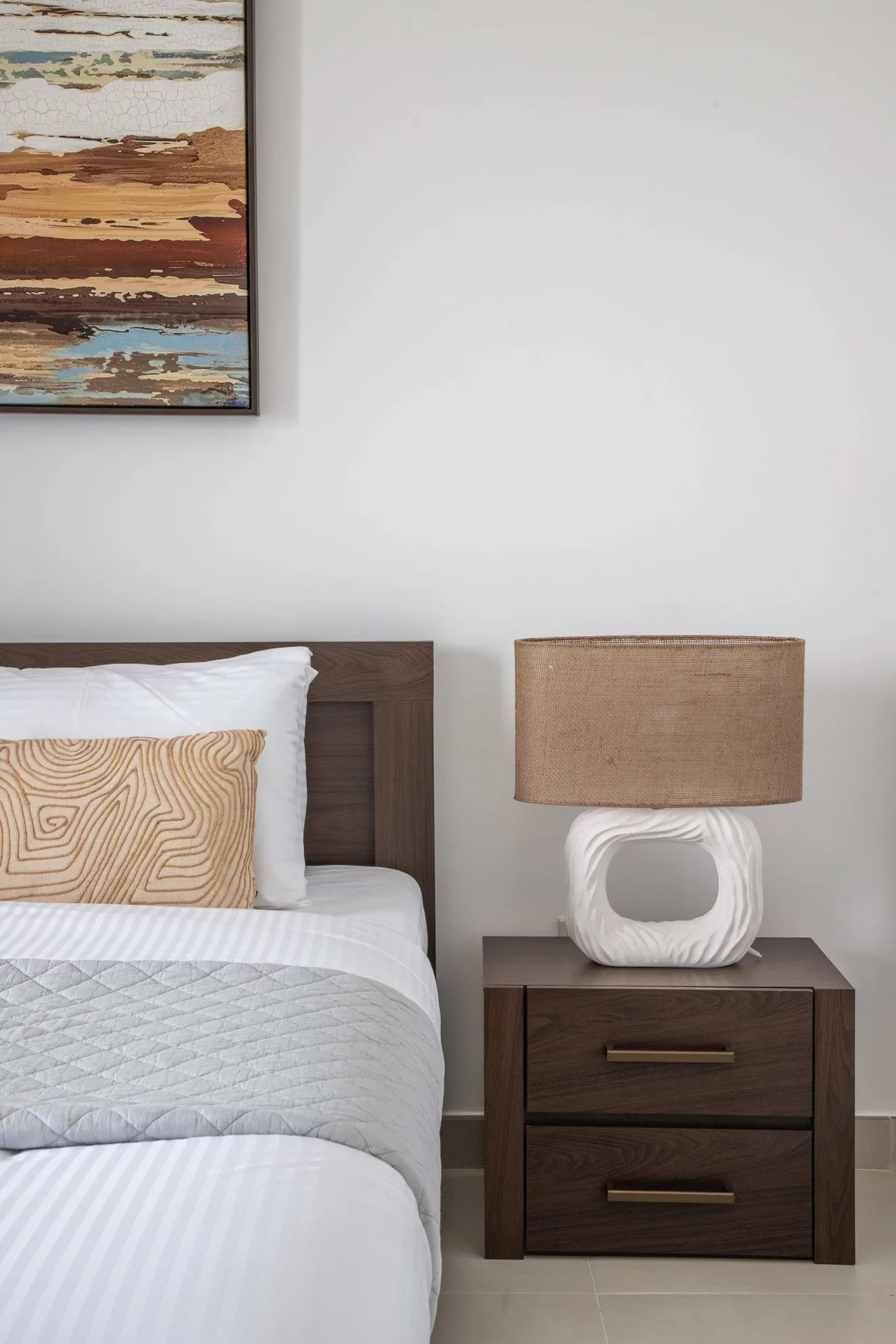 Un dormitorio con una cama bien hecha y una mesita de noche con una lámpara.