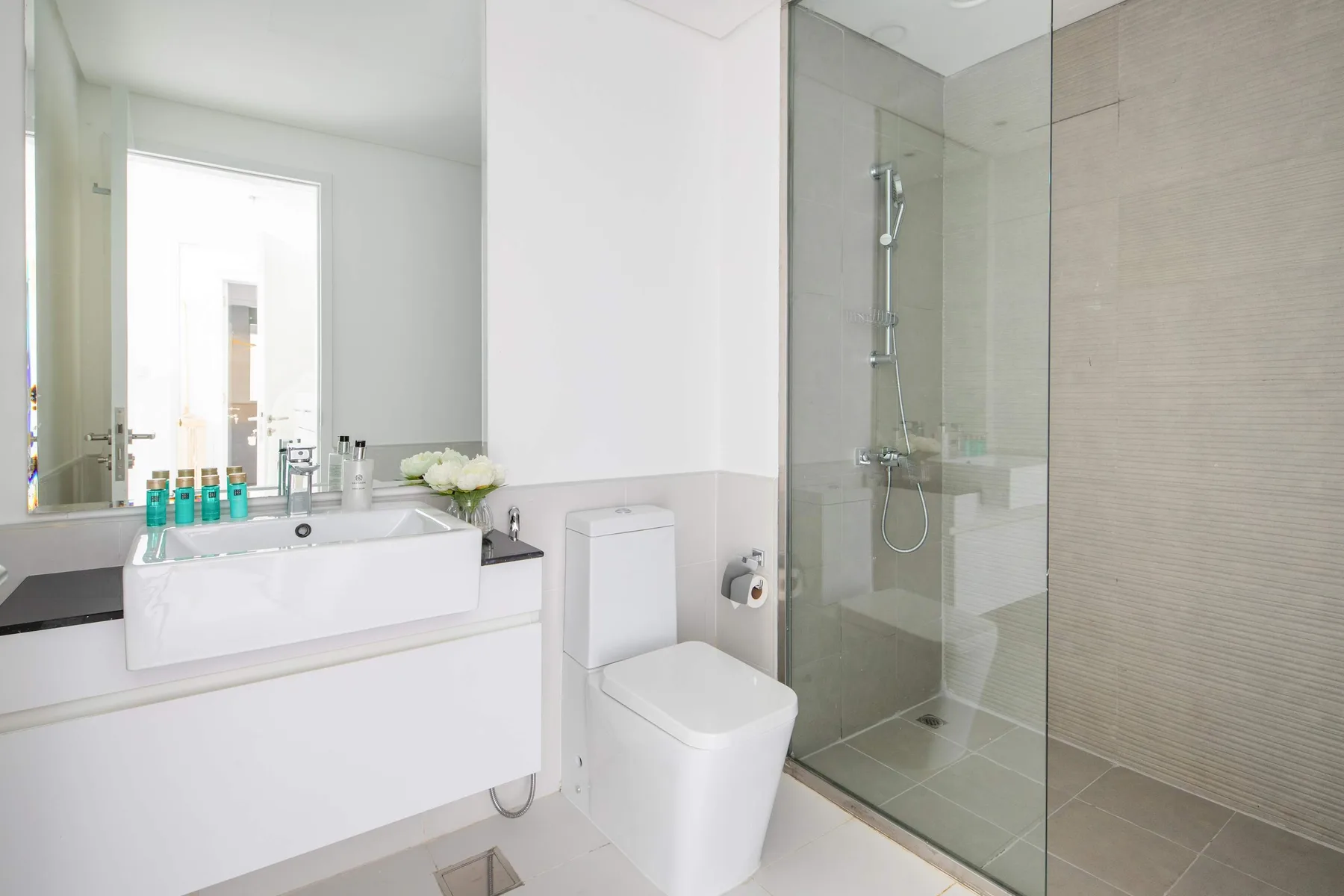 Un baño luminoso con lavabo, inodoro y ducha con mampara de vidrio.
