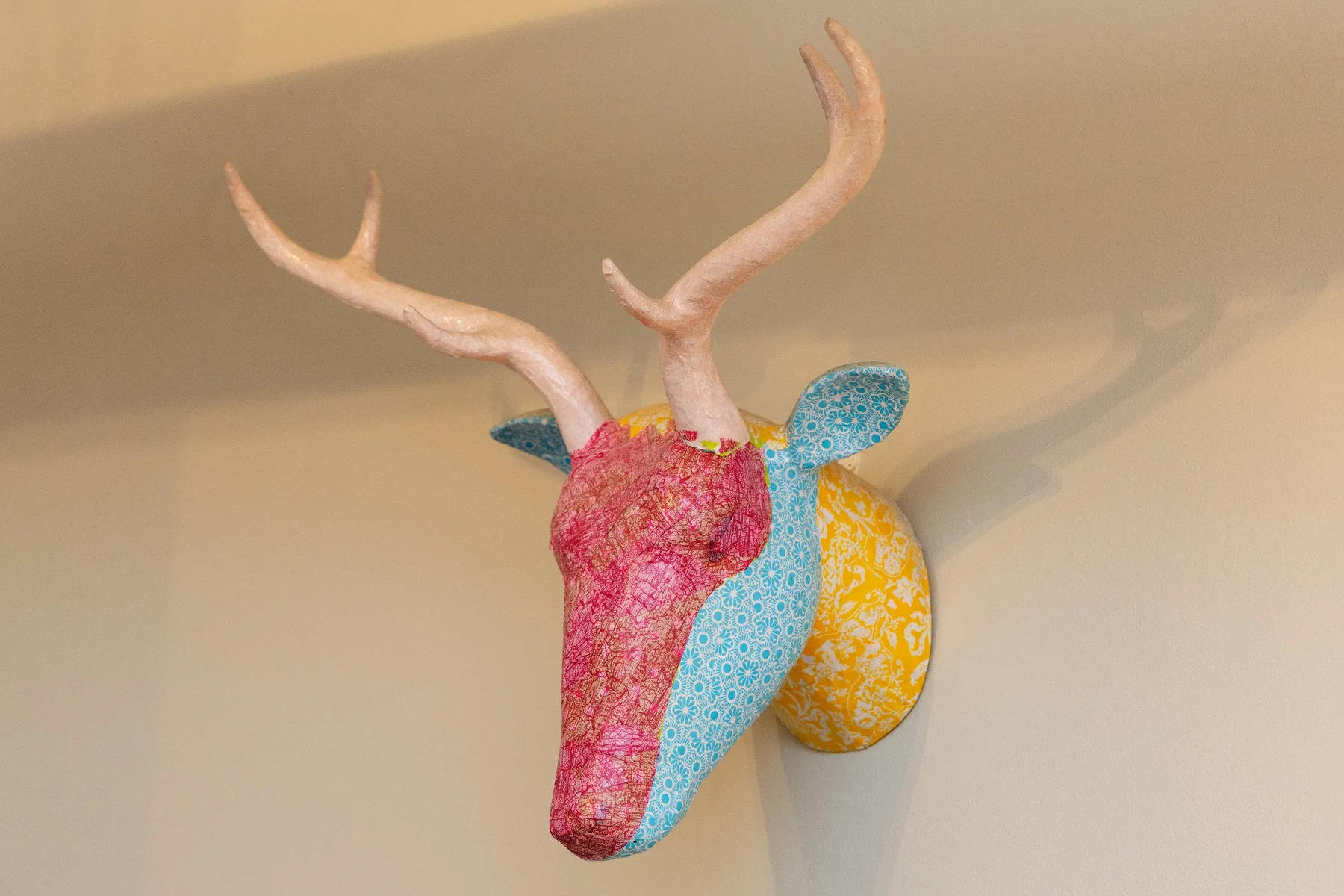 A colorful decorative deer head with antlers is mounted on a light wall.