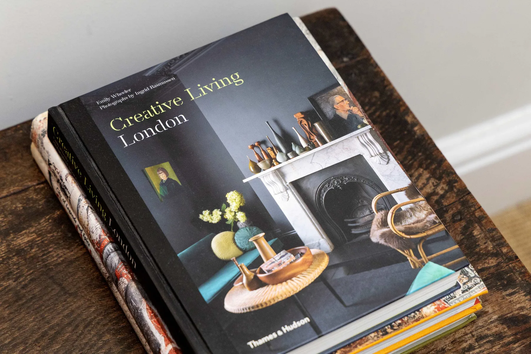 A stack of design books rests on a dark wooden table.