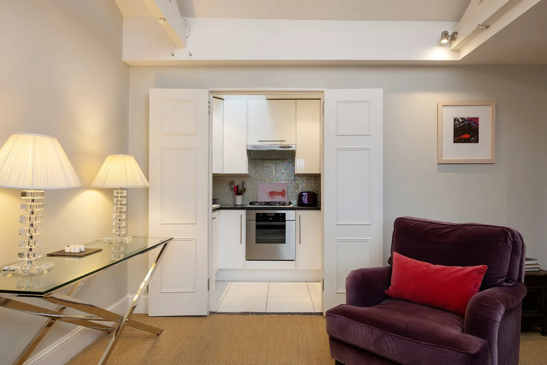 A living room with a burgundy armchair and a view into the kitchen.