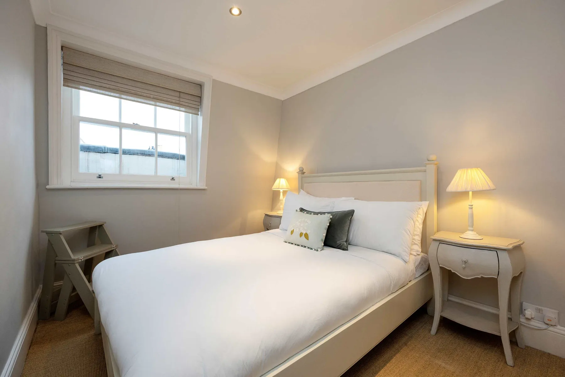 A bright bedroom with a neatly made bed and bedside lamps.