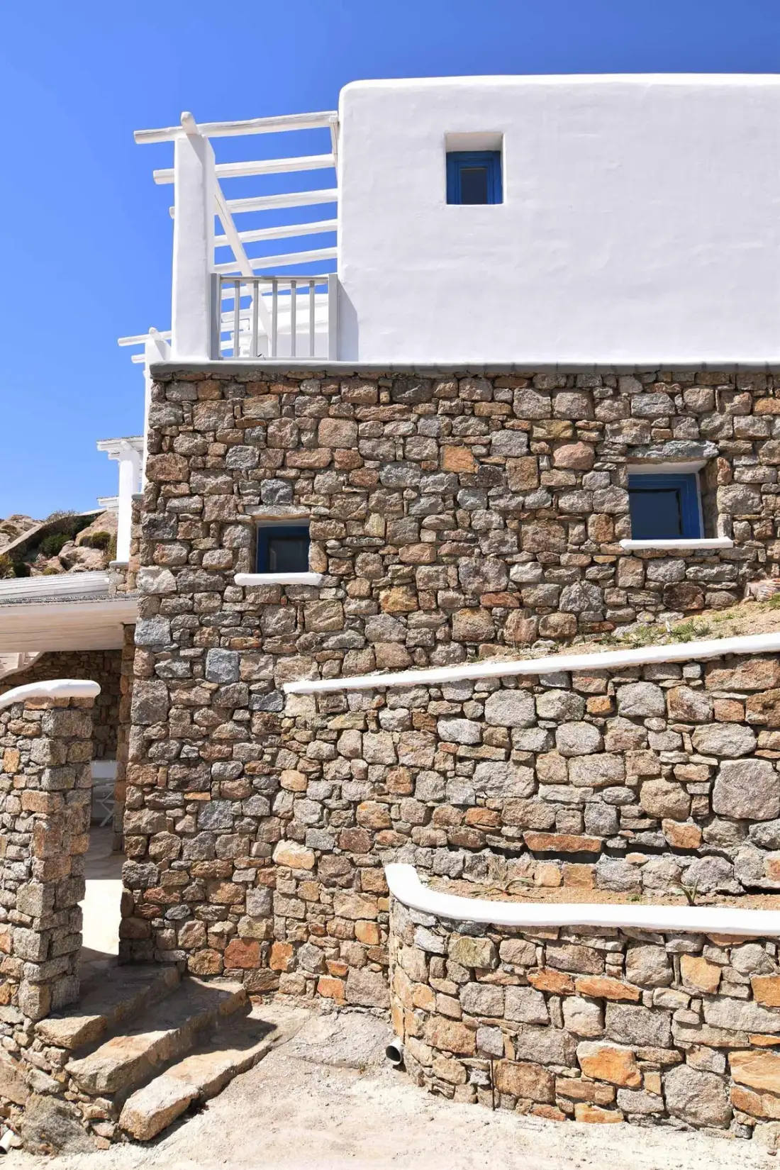 A stone exterior wall and curved steps beneath a white upper facade.