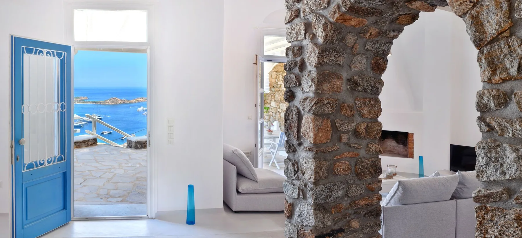 A bright lounge opens onto a sea view through a blue doorway.