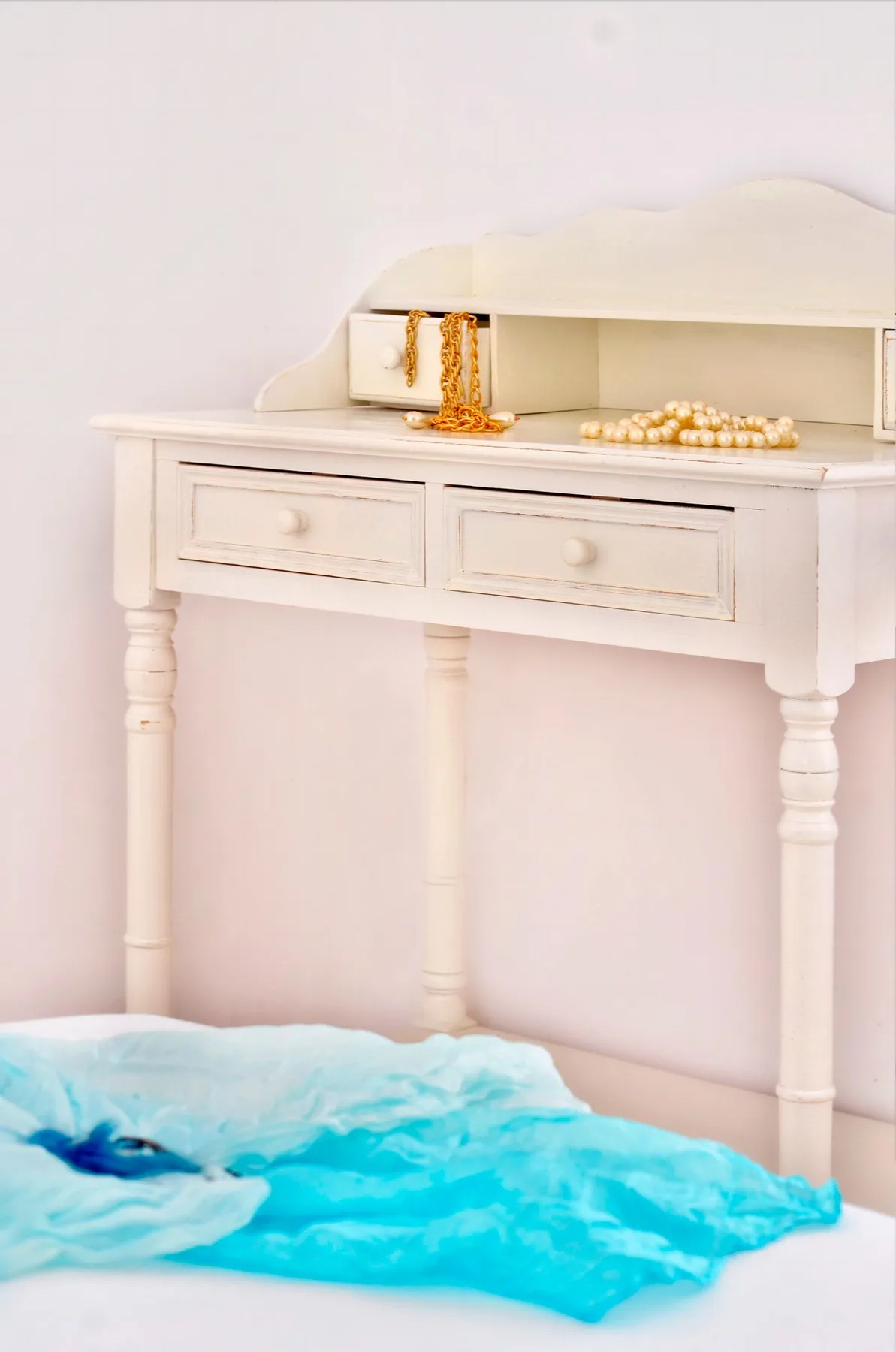 A white dressing table stands above bright turquoise fabric.