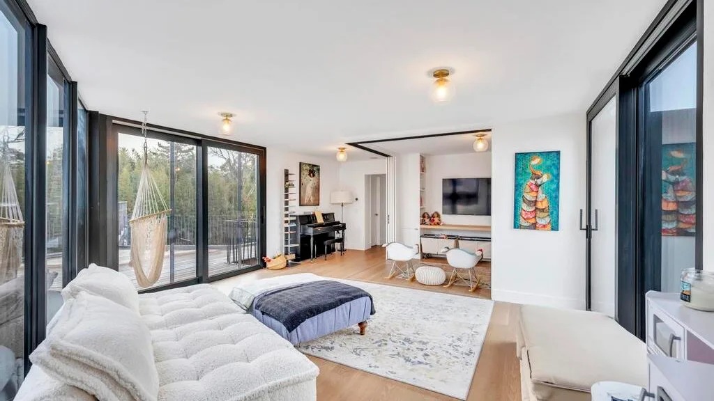 Una sala luminosa con ventanales, una zona de asientos blanca y una alfombra grande.
