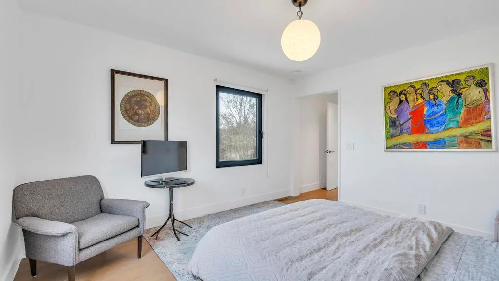 Un dormitorio luminoso con una cama, un sillón y arte colorido en la pared.