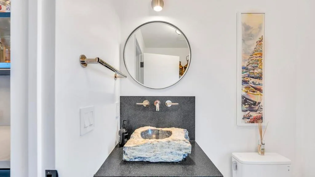 Un lavabo de baño con espejo redondo y un lavamanos sobrepuesto.