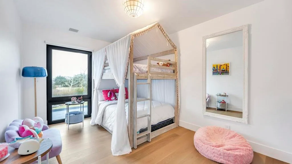 Un dormitorio luminoso con una cama litera con dosel y una ventana grande.
