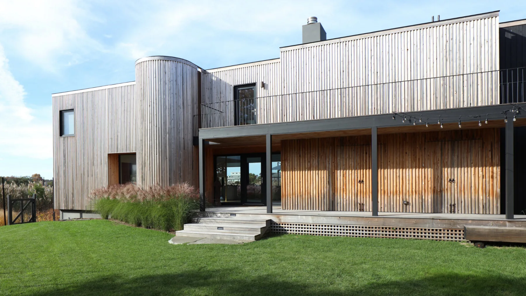 Una casa moderna con exterior revestido de madera y césped verde.