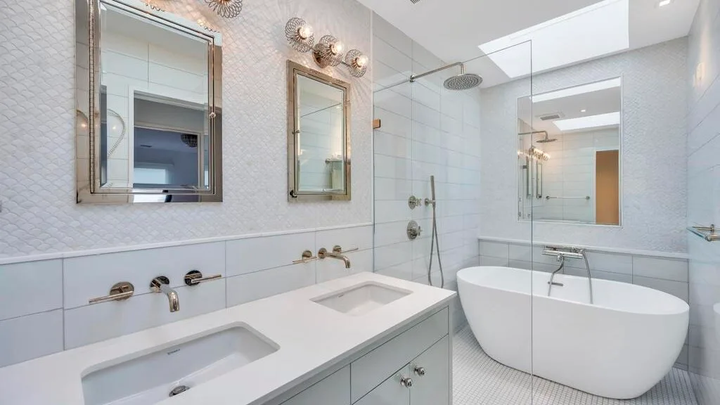 Un baño luminoso con un lavabo doble y una bañera exenta.