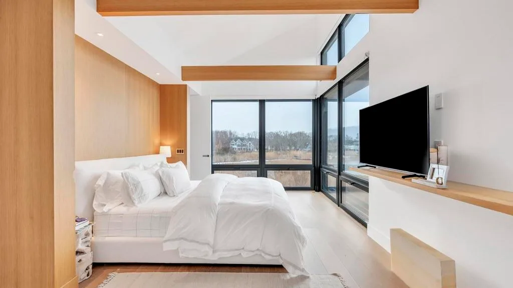 Un dormitorio luminoso con una cama junto a grandes ventanas y un televisor.