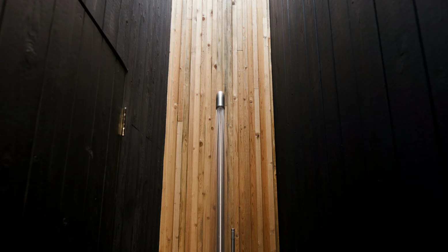 Una zona de ducha tiene una ducha de mano montada en una pared clara revestida de madera.