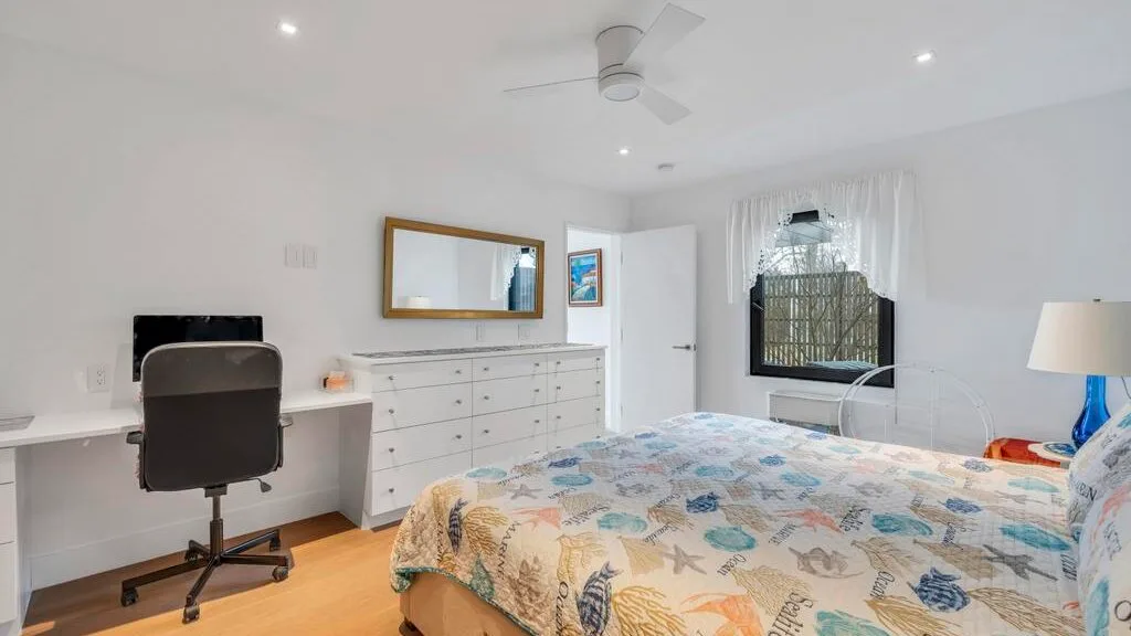 Un dormitorio con cama, escritorio y cómoda bajo un ventilador de techo.