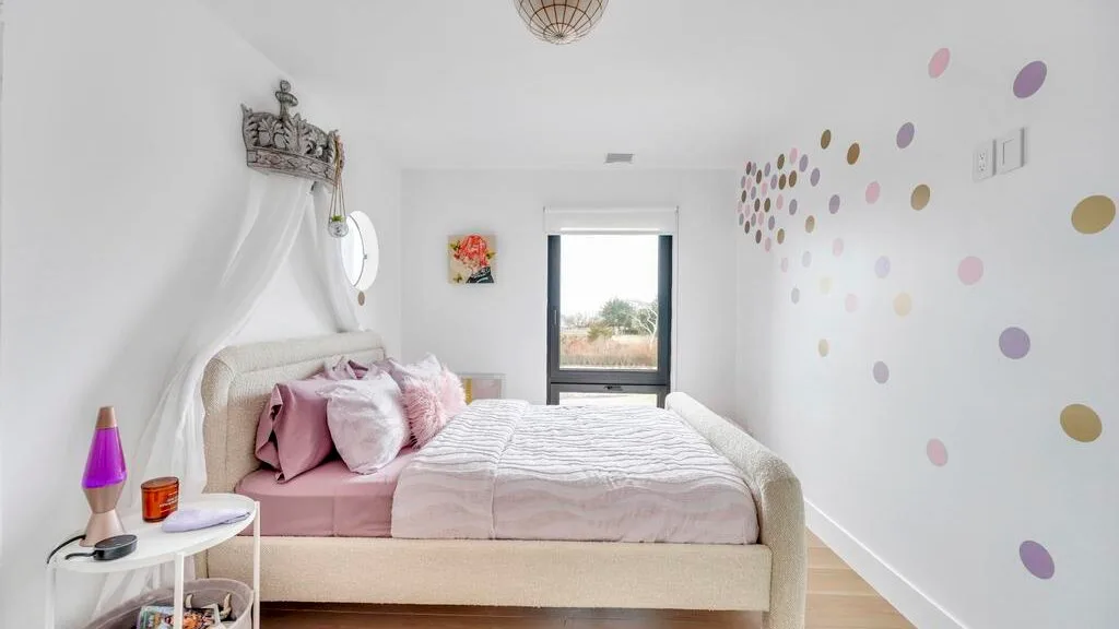 Un dormitorio con una cama, almohadas rosas y puntos de colores en la pared.