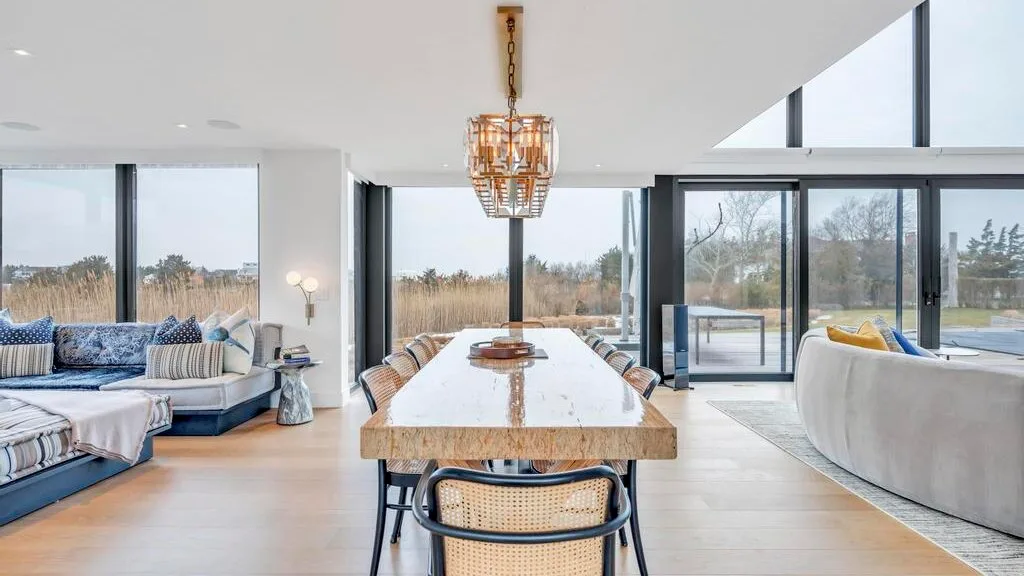 Una luminosa sala de estar y comedor de planta abierta, con grandes ventanales y una mesa larga.