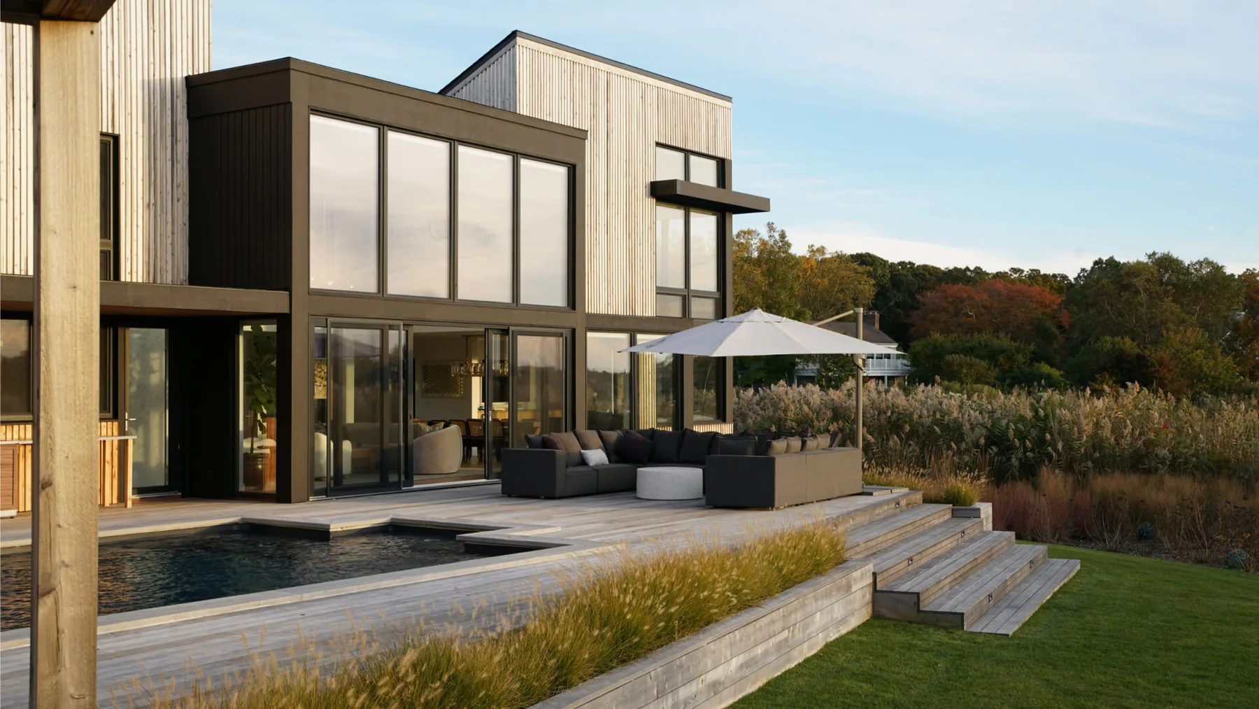 Una casa moderna da a una terraza de madera con piscina y asientos al aire libre.