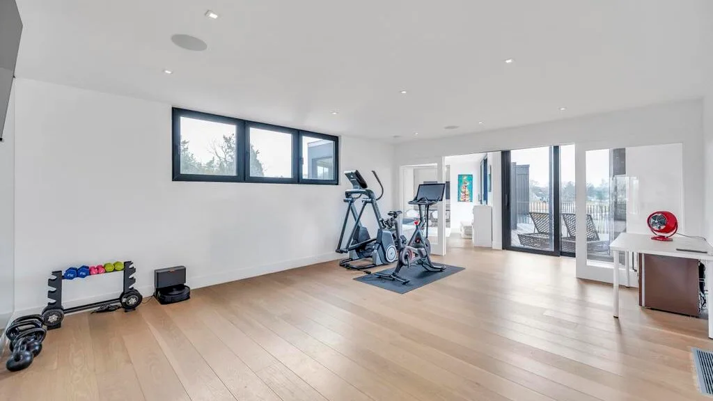 Una luminosa sala de ejercicio con equipos de cardio y ventanas grandes.