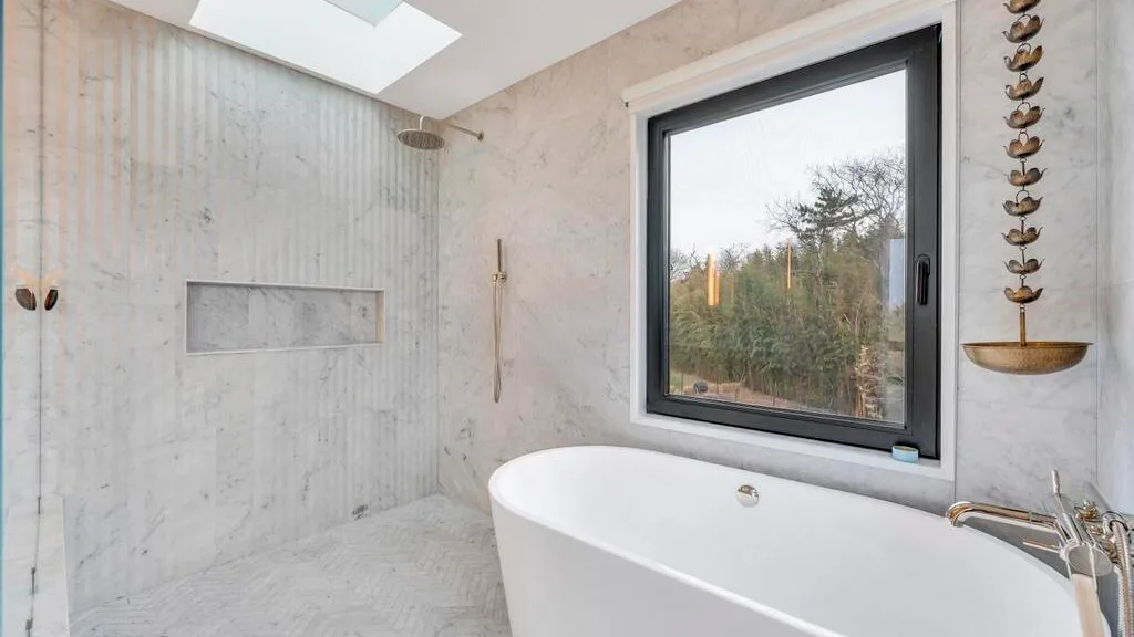 Un baño luminoso con una bañera exenta junto a una ventana grande.