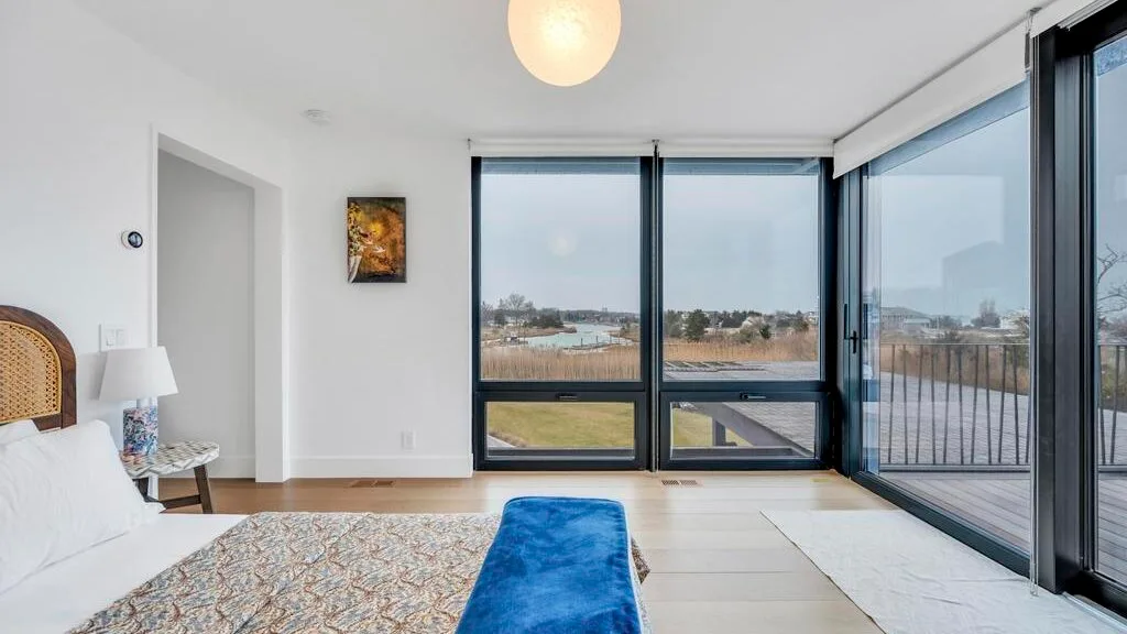 Un dormitorio luminoso con una cama junto a grandes ventanas con vistas al agua.