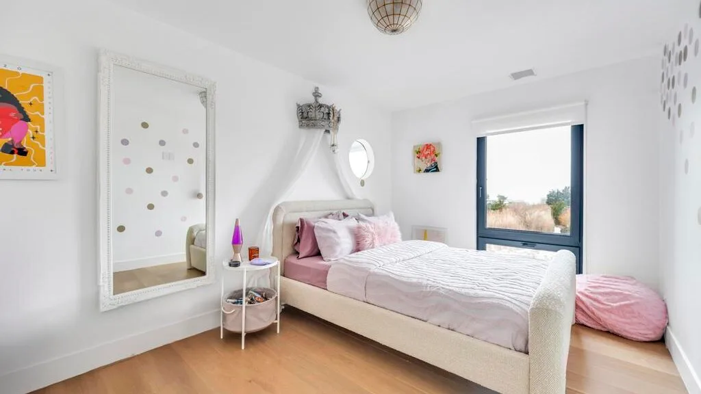 Un dormitorio luminoso con una cama, ropa de cama rosa y una ventana grande.
