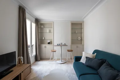 A bright living room with teal seating, a television, and a small dining table.
