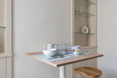 A small dining table with place settings sits beneath glass display shelves.