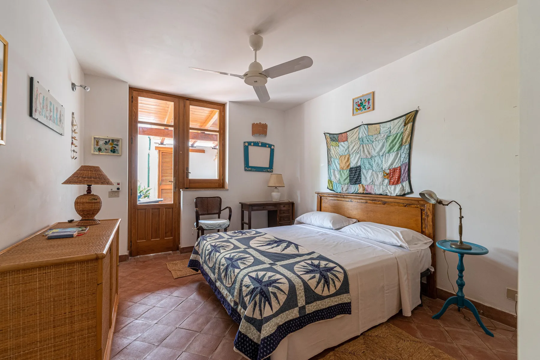 A bedroom with a double bed, patterned bedspread, and wooden door.