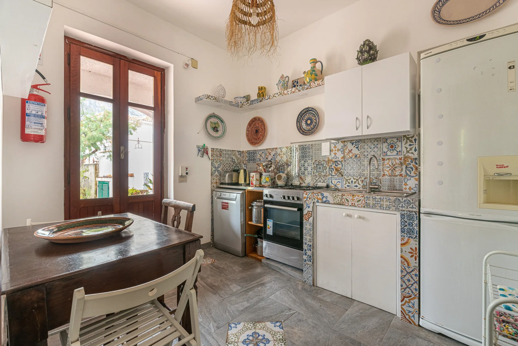 A tiled kitchen with a stove, cabinets, and a dining table by the window.
