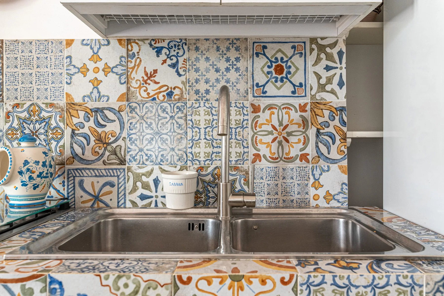 A kitchen sink sits beneath a wall of colorful patterned tiles.