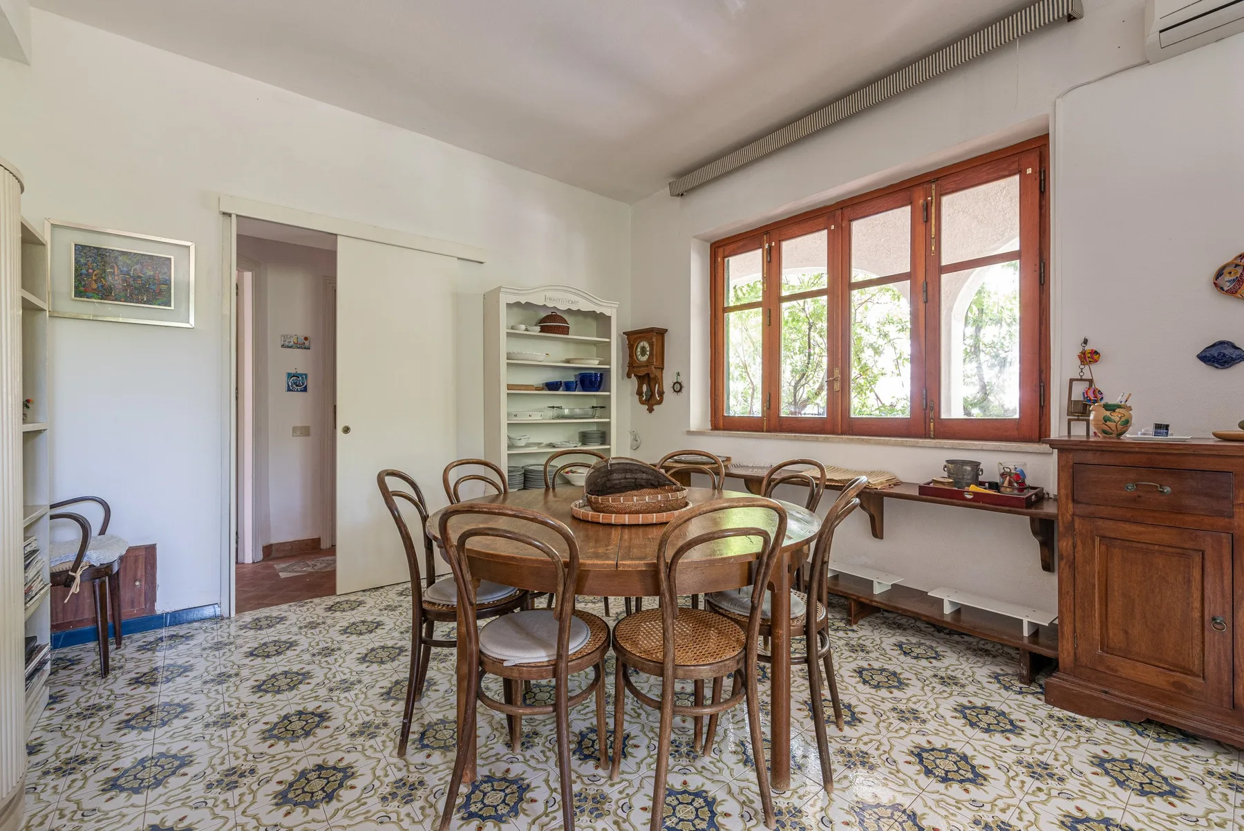 A dining room with a wooden table and chairs beside large windows.
