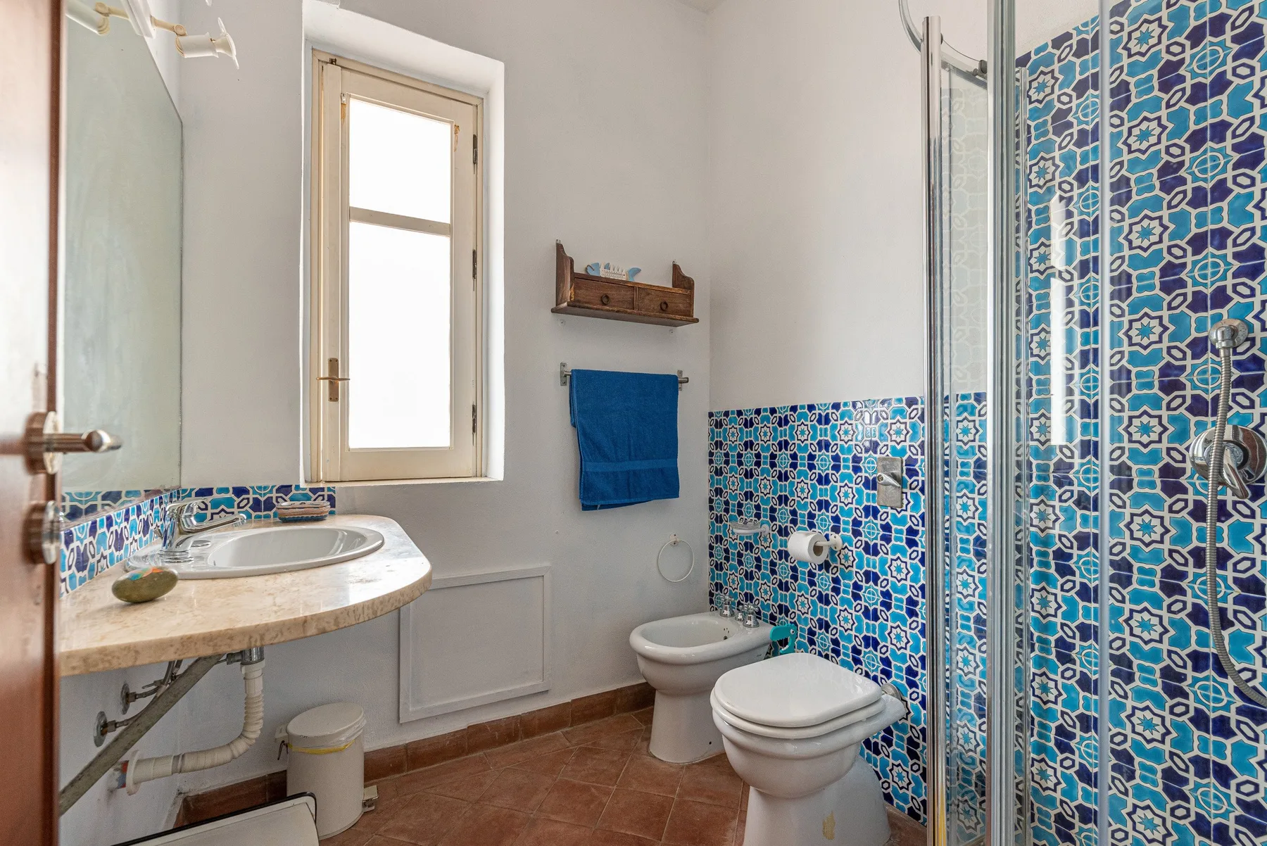 A bathroom with a sink, toilet, and blue patterned tile.