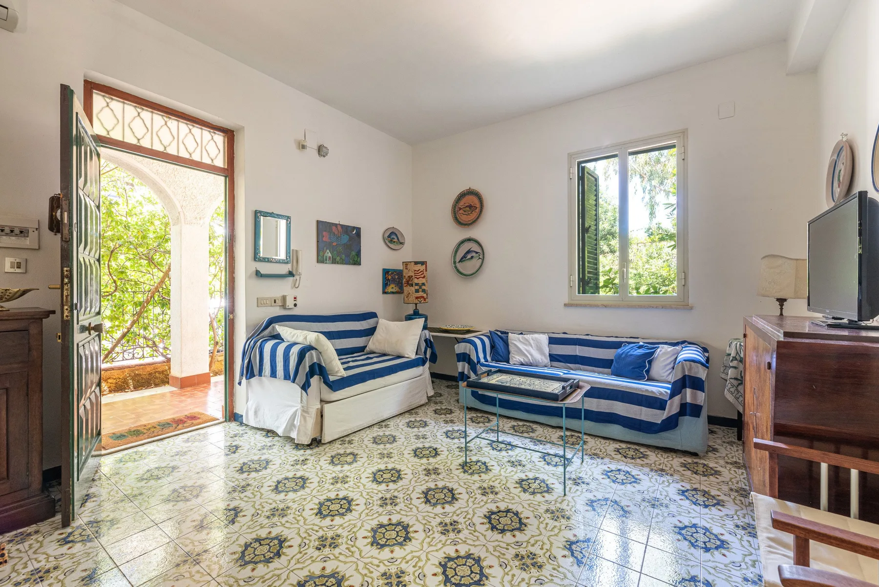 A living room with blue-and-white seating and an open doorway to a sunlit balcony.