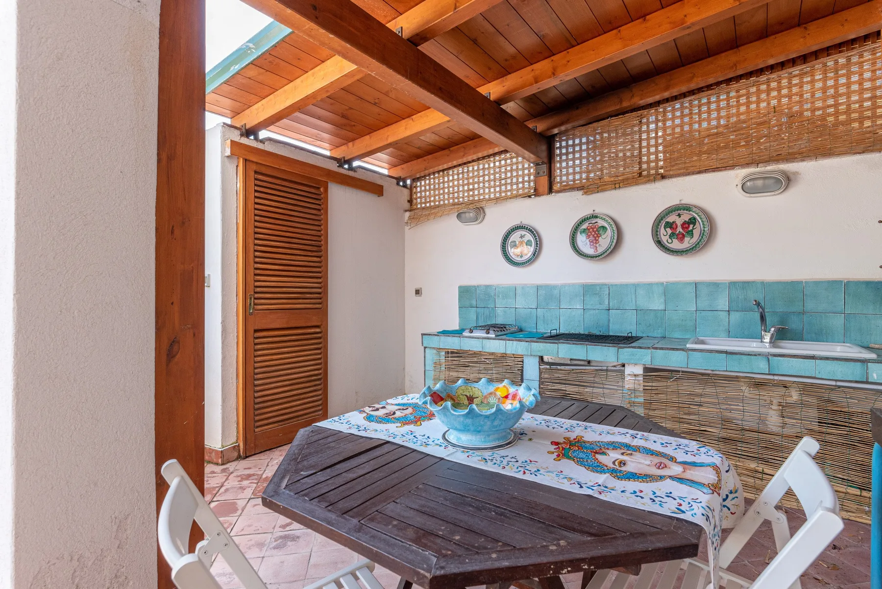 A covered outdoor dining area with a table beside a tiled counter and sink.