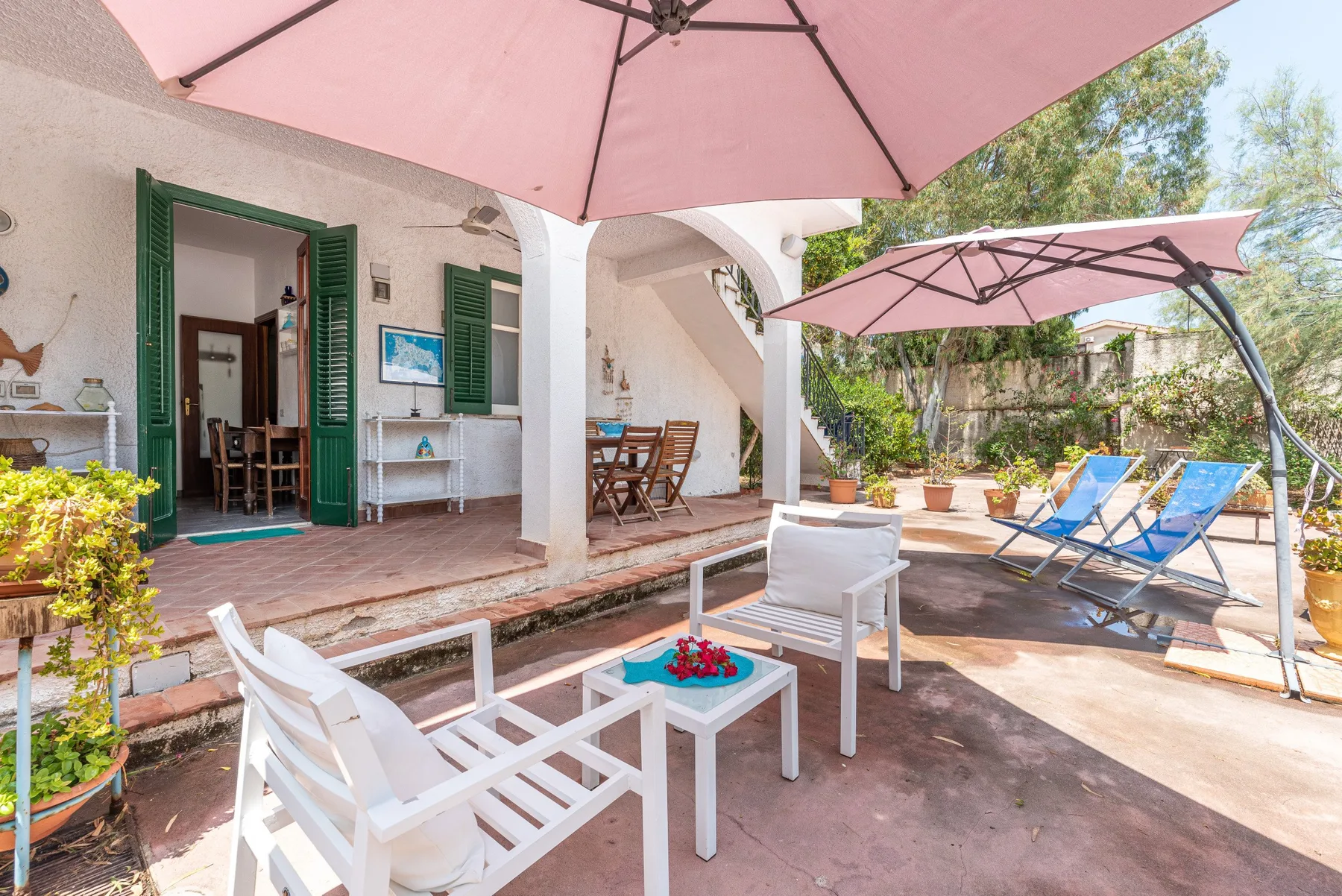 A sunny outdoor patio with seating, pink umbrellas, and blue lounge chairs.