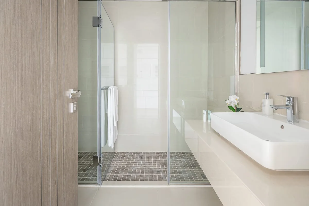 A bright bathroom with a glass shower and a long white sink.