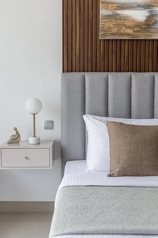 A bedroom with a neatly made bed beside a wall-mounted nightstand.