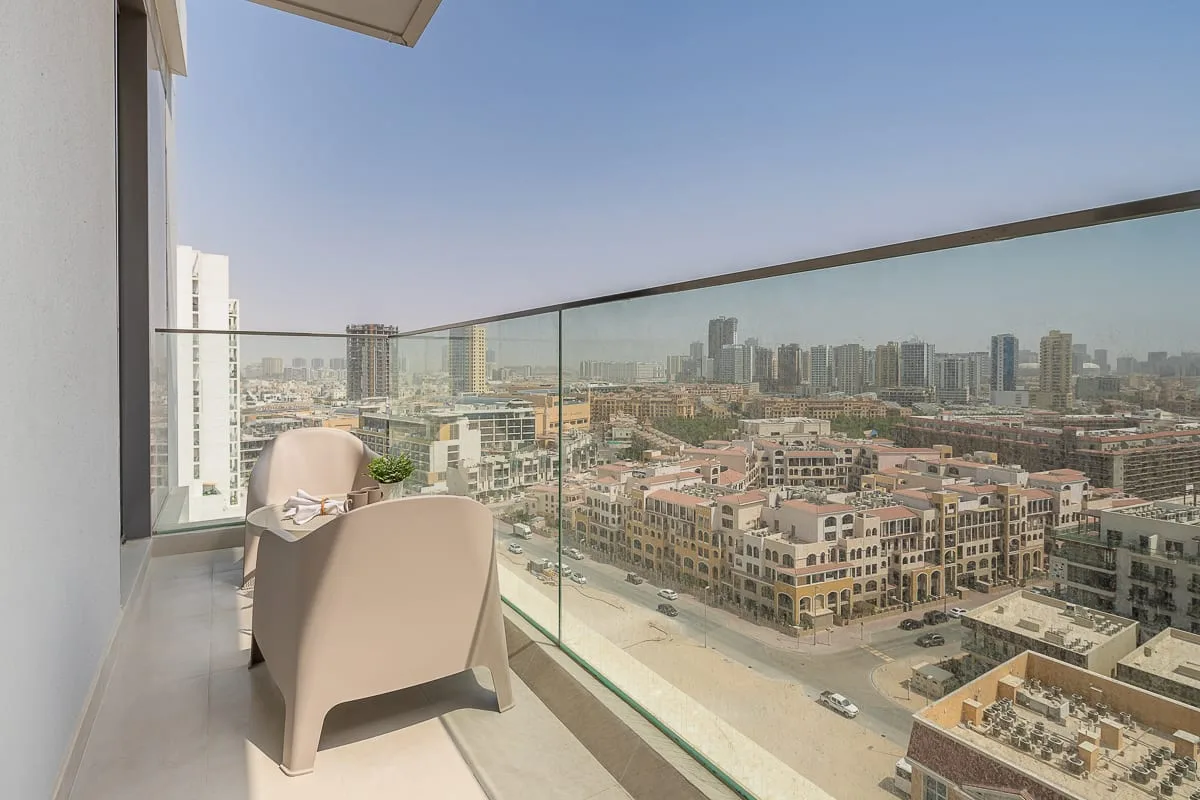 A balcony overlooks city buildings, with seating beside a glass railing.