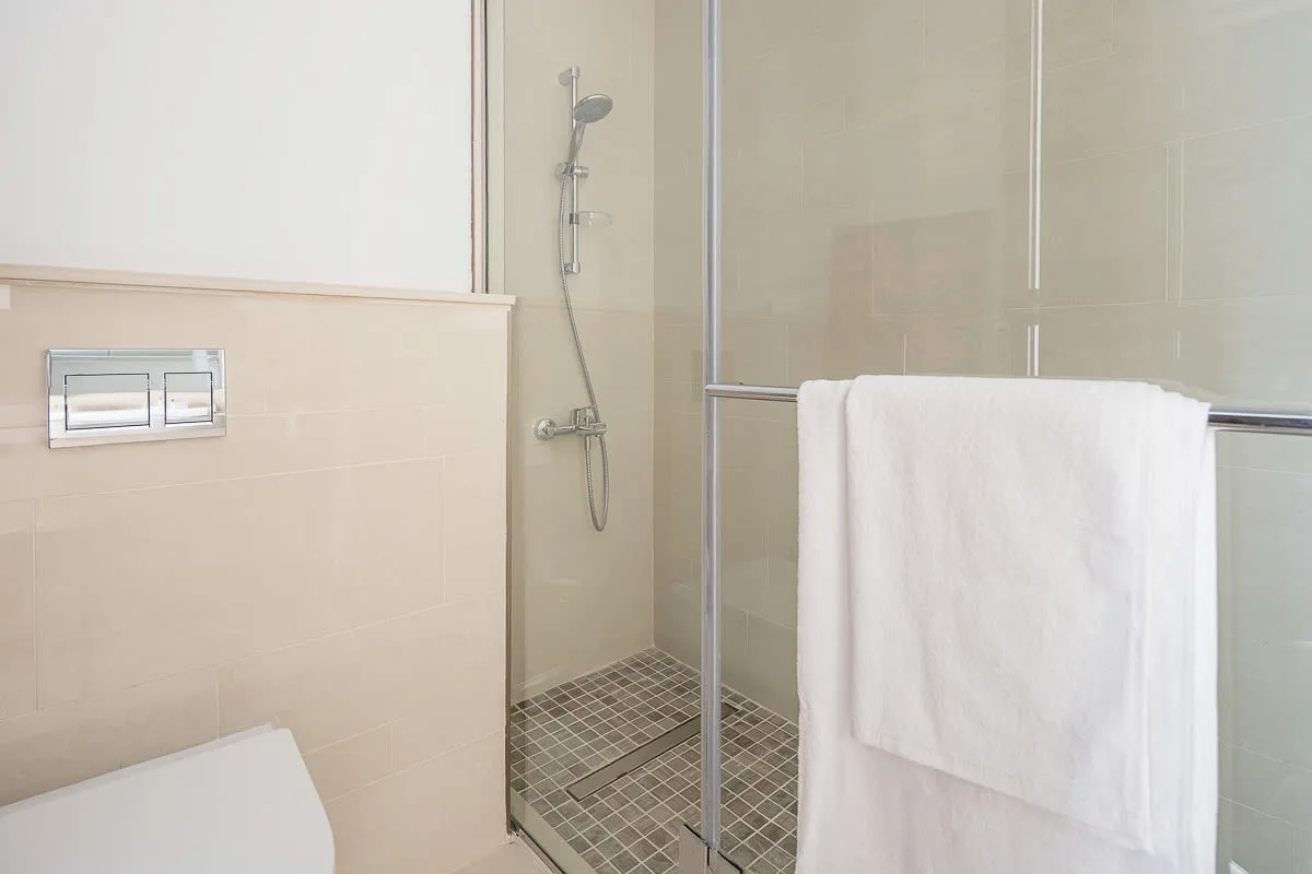 A tiled bathroom shower with a white towel hanging on the glass partition.