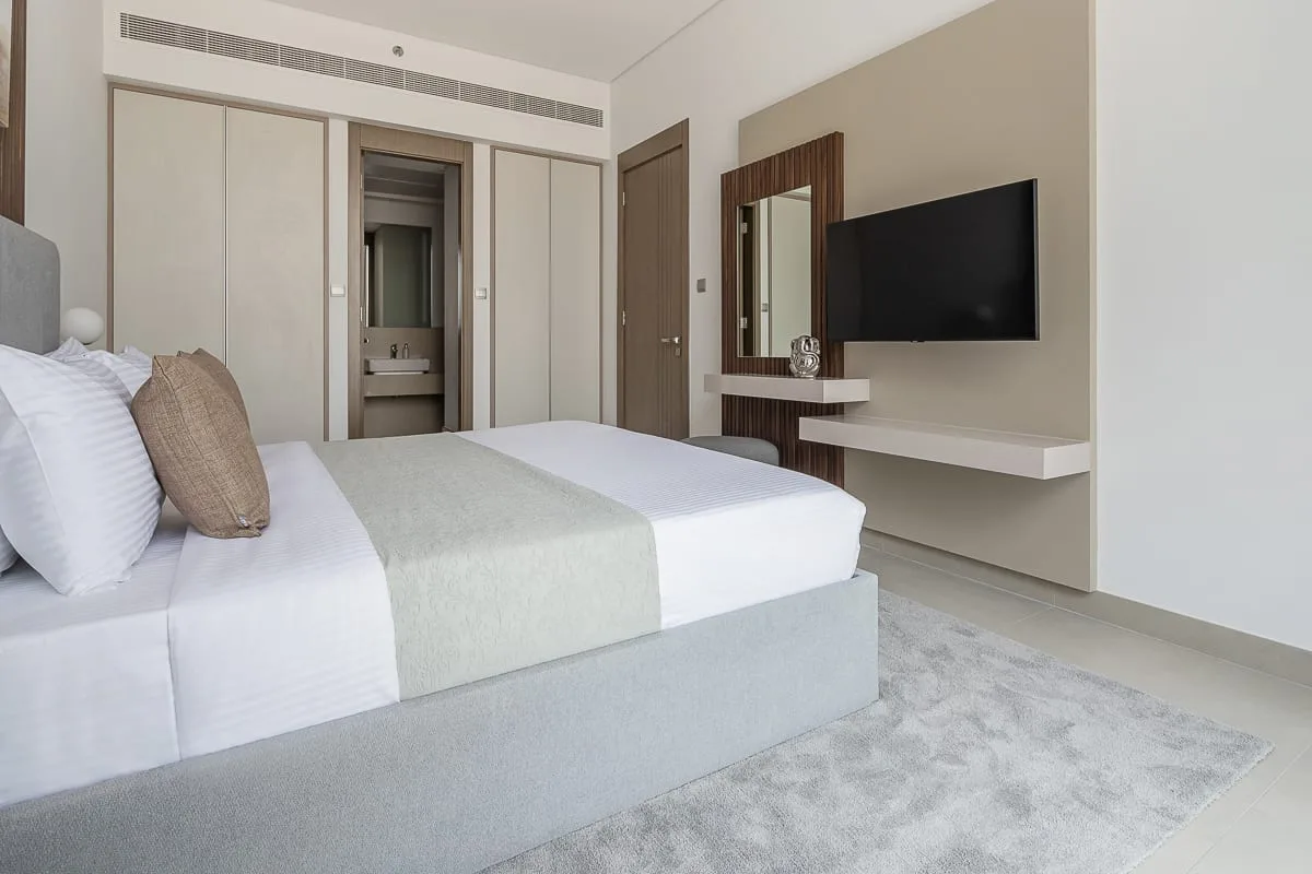 A bright bedroom with a neatly made bed and a wall-mounted television.