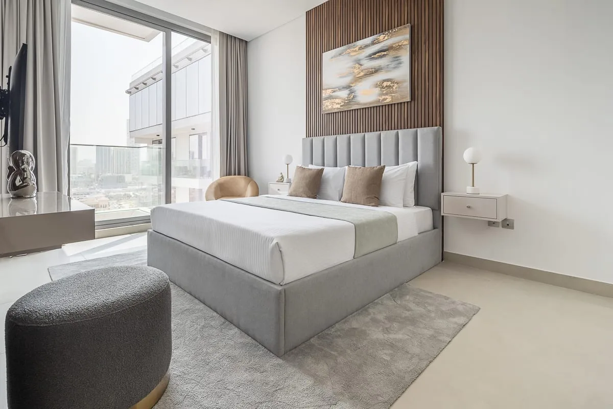 A bright bedroom with a large bed beside floor-to-ceiling windows.