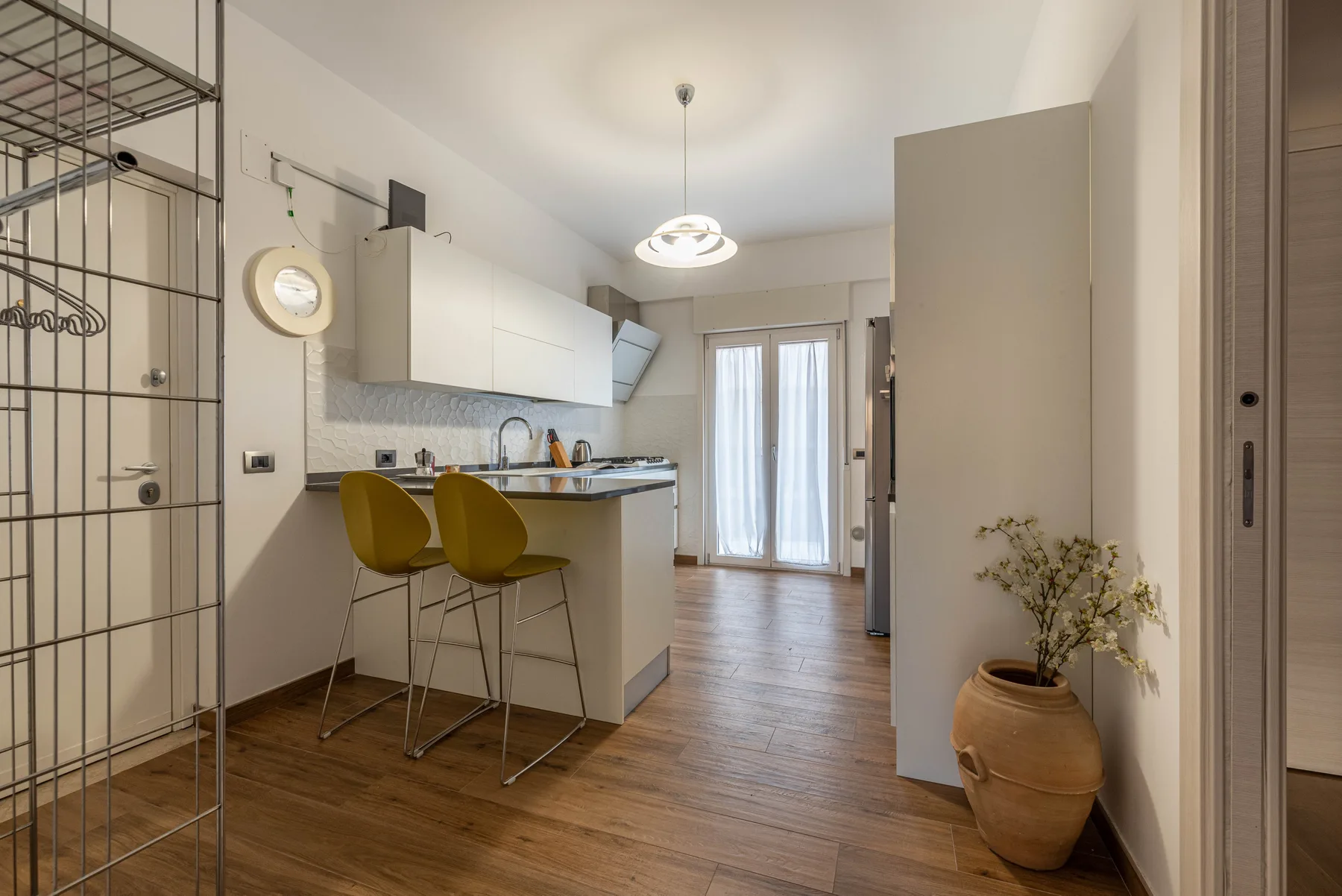 A bright kitchen with a breakfast counter and two stools, opening onto a dining area.