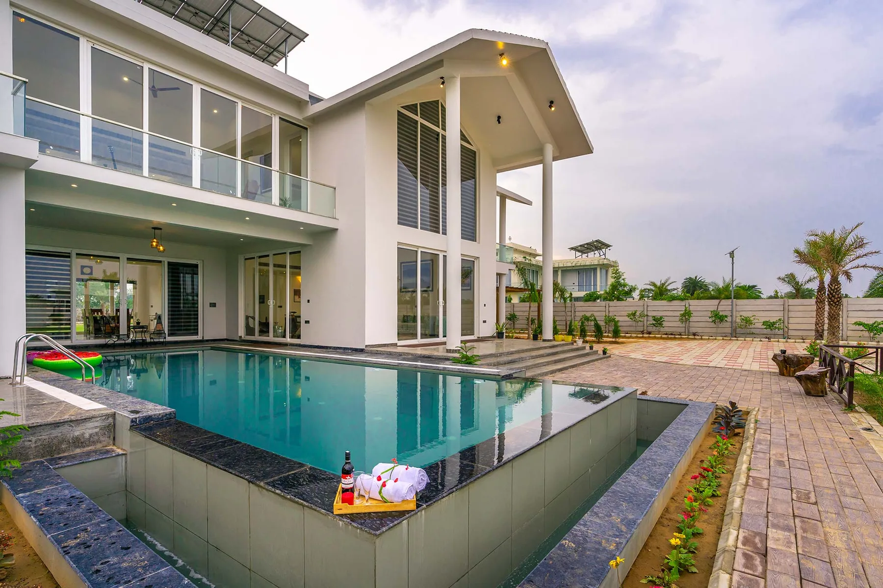 A modern house stands beside a swimming pool and paved patio.