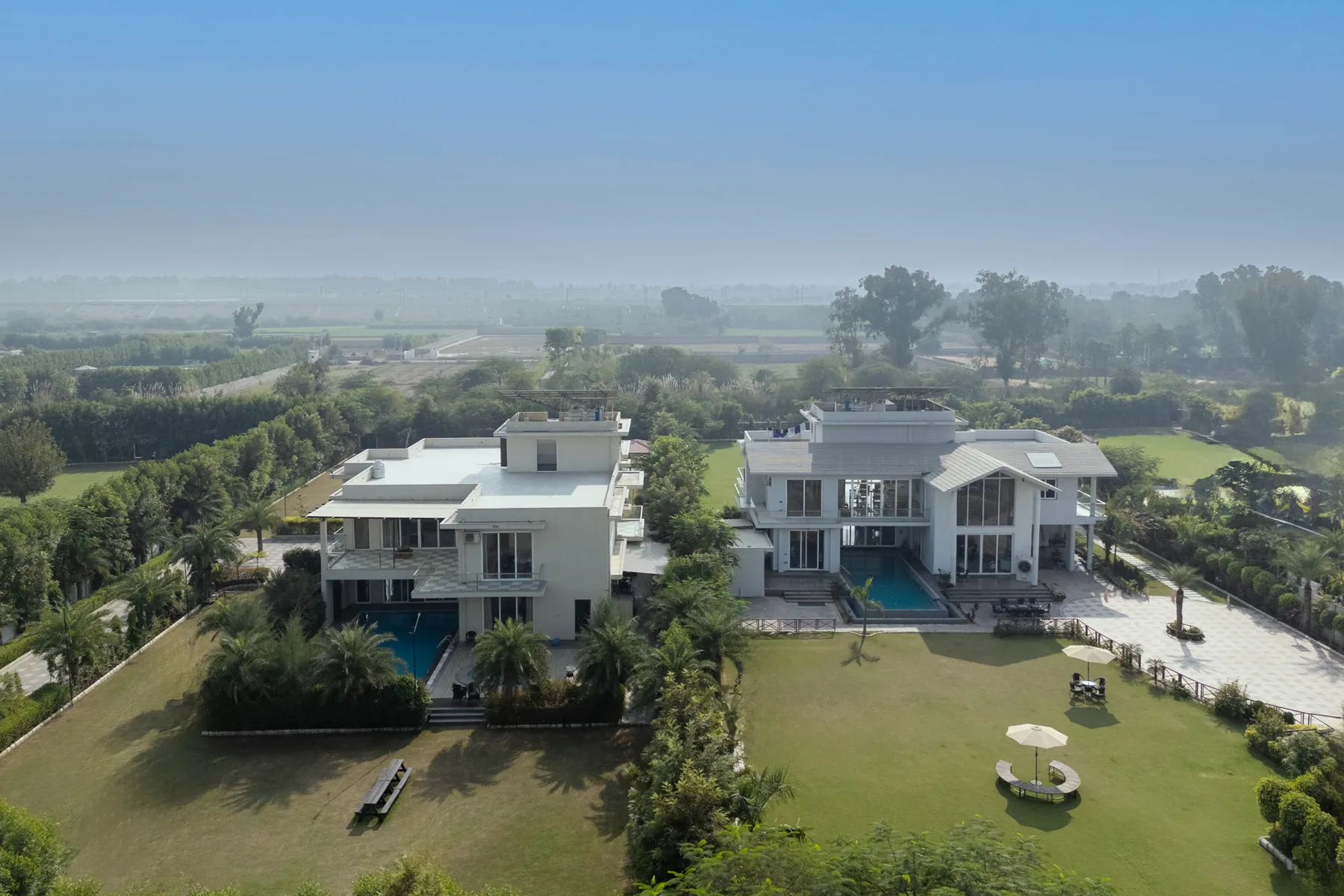 Vista aérea de dos casas modernas junto a un césped y piscinas.