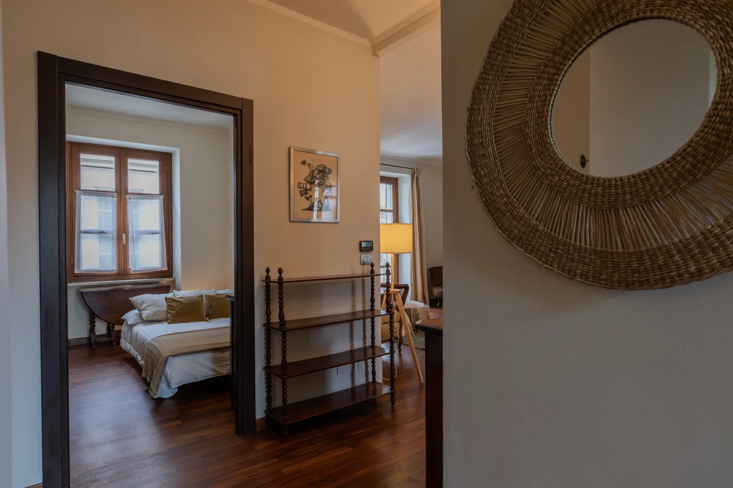 Se ve un dormitorio a través de una puerta, junto a un estante y un espejo redondo.