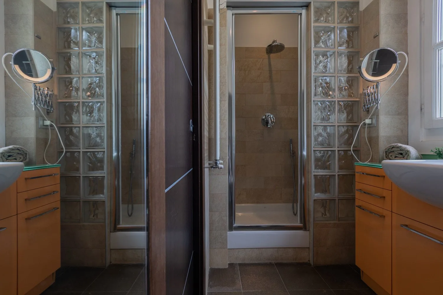 Un baño alicatado con una ducha de vidrio y muebles de lavabo a ambos lados.